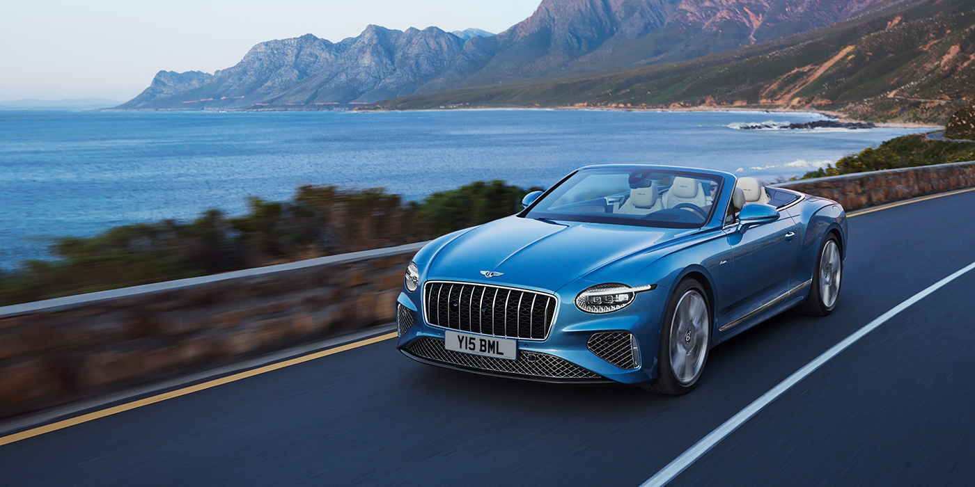 Bentley Firenze New Bentley Continental GTC Azure convertible in Light Windsor blue paint with 22 inch Azure wheels and chrome grill, driving dynamically by the sea