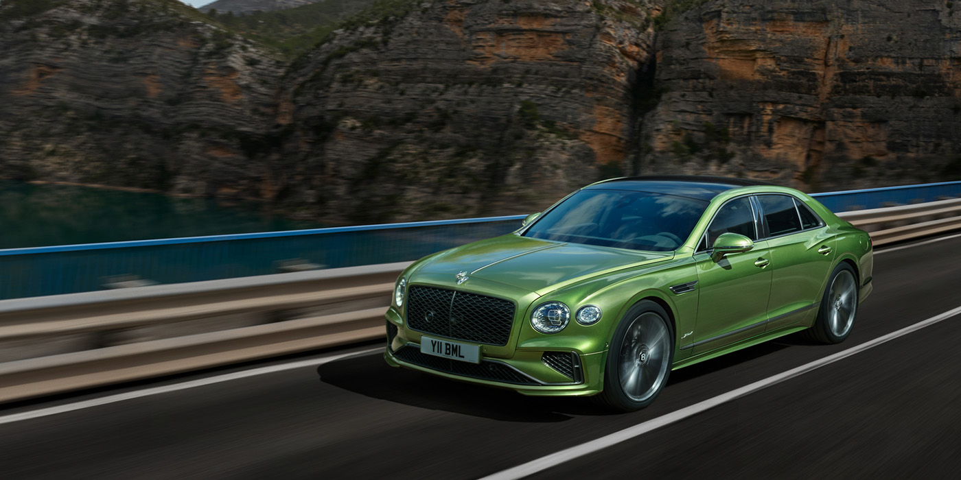 Bentley Firenze Bentley New Flying Spur Speed v8 hybrid sedan driving dynamically on a mountain road in Tourmaline Green paint