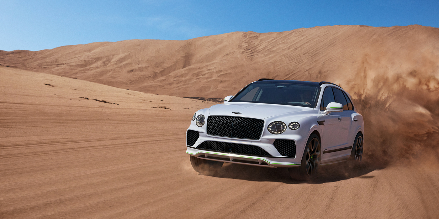 Bentley Firenze Bentley Bentayga Speed SUV front three quarter in Snow Quarts Pearlescent by Mulliner white paint driving dynamically through the desert