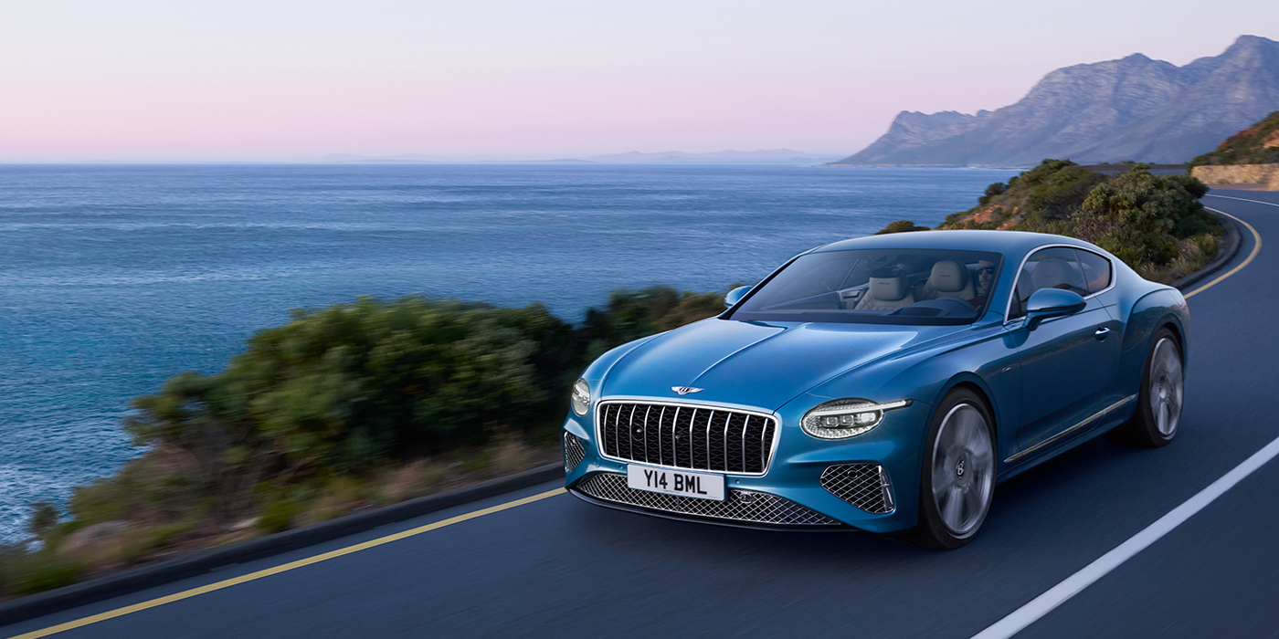 Bentley Firenze New Bentley Continental GT Azure coupe in Light Windsor blue paint with 22 inch Azure wheels and chrome grill, driving dynamically by the sea