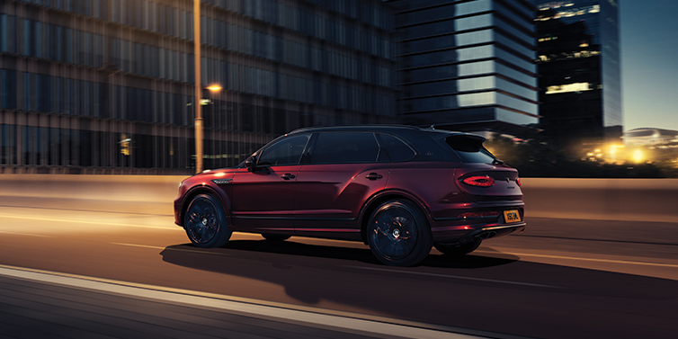 Bentley Firenze Bentley Bentayga Extended Wheelbase Mulliner SUV in Cricket Ball red paint driving dynamically in city at night